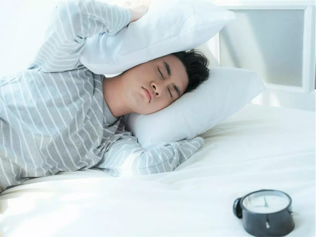 枕で耳を抑えている男性