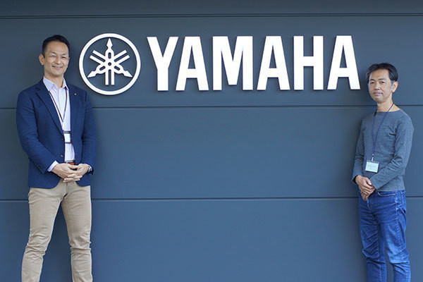 YAMAHAロゴ前に立つ瀬尾 達也 氏と藤木 大輔 氏